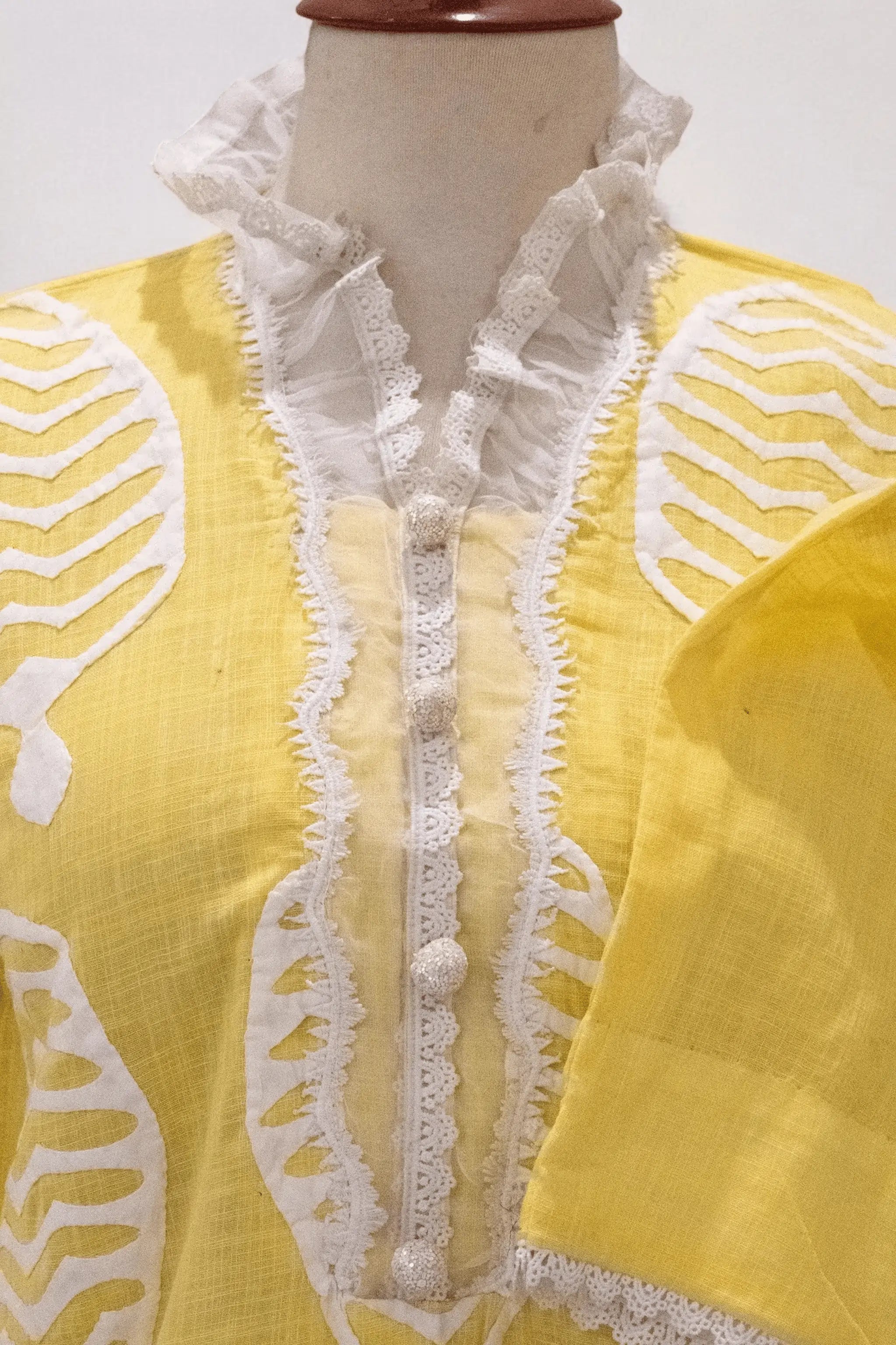 Front design of Apachi unstitched shirt featuring fabric buttons and lace finishing.